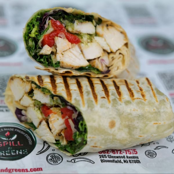 Two grilled chicken wraps, one cut in half, filled with chicken, lettuce, and red peppers.