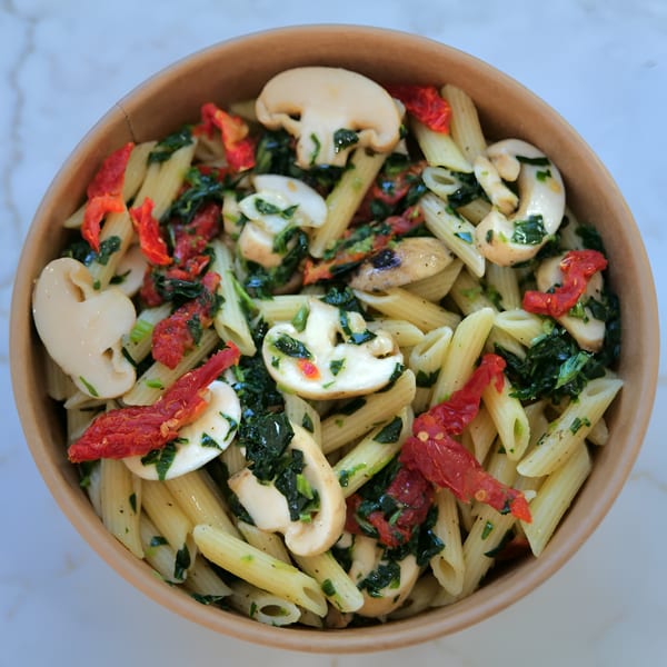 Penne pasta with mushrooms, sun-dried tomatoes, and spinach in a brown bowl from Grill and Greens.