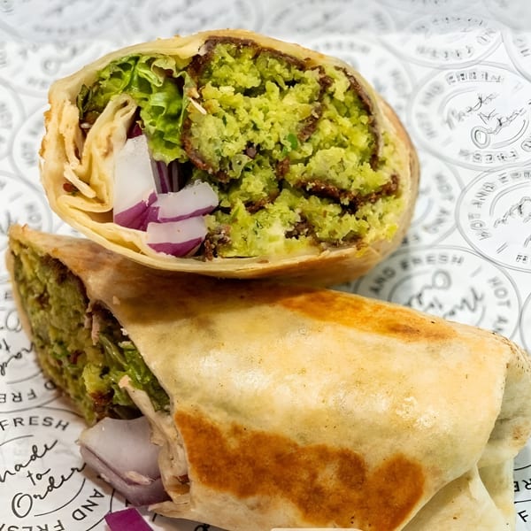 Two halves of a healthy falafel wrap with lettuce and red onion on branded paper.