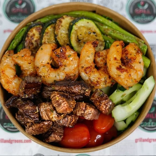 Grilled shrimp, steak, zucchini, asparagus, cucumbers, and tomatoes in a bowl.