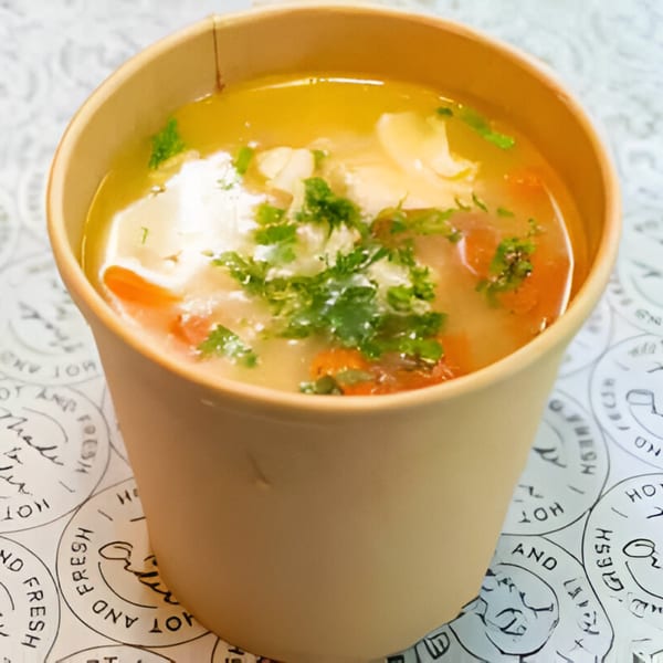 Healthy chicken and vegetable soup in a brown paper cup, garnished with fresh parsley.