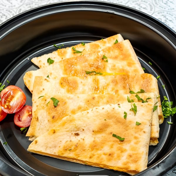 Golden-brown quesadillas garnished with parsley and cherry tomatoes in a black bowl.