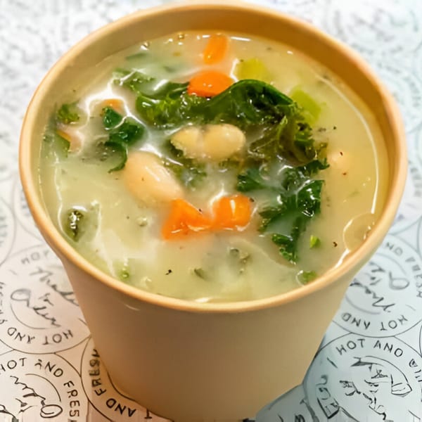 Creamy white bean and kale soup with carrots in a paper cup from Grill and Greens.