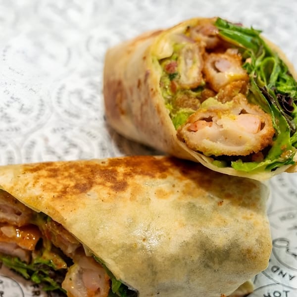 Two halves of a crispy shrimp and lettuce wrap on patterned white paper.