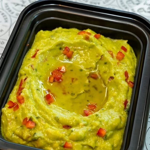 Close-up of vibrant green guacamole with red bell pepper pieces and a pool of olive oil.
