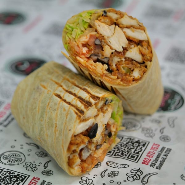 Two grilled chicken wraps, one cut open to show lettuce, black beans, and chicken, on patterned paper.
