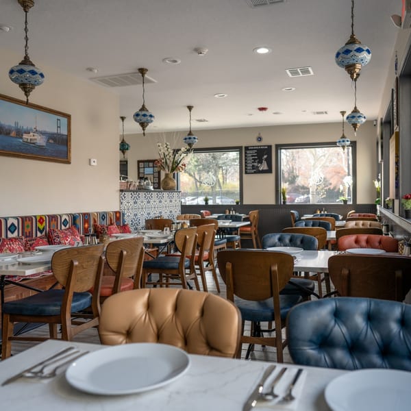 Interior of Grill and Greens restaurant with colorful patterned banquettes, wooden chairs, and decorative blue lamps.