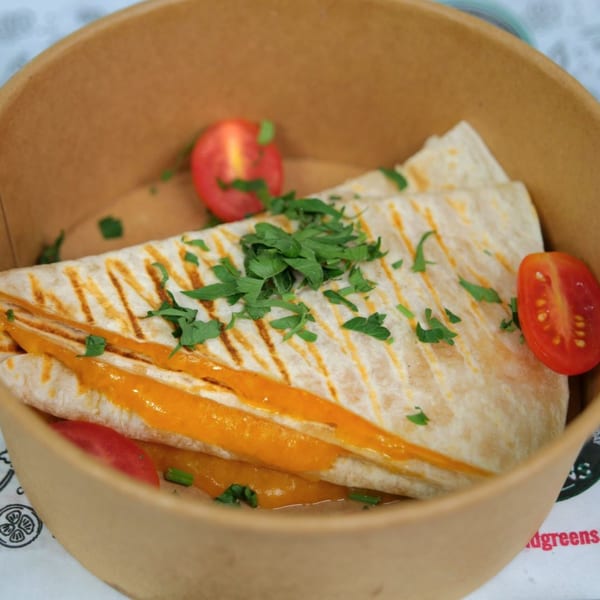 Grilled quesadilla with melted cheese, topped with fresh parsley and cherry tomato halves in a bowl.