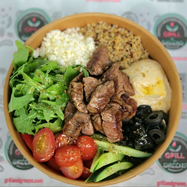 A vibrant bowl of grilled beef, arugula, cherry tomatoes, olives, hummus, feta, and quinoa.