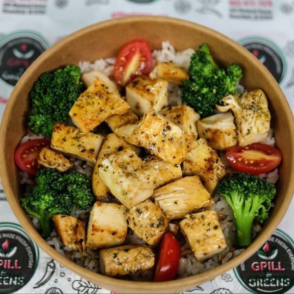 Grilled chicken, broccoli, and cherry tomatoes served over rice in a brown paper bowl.