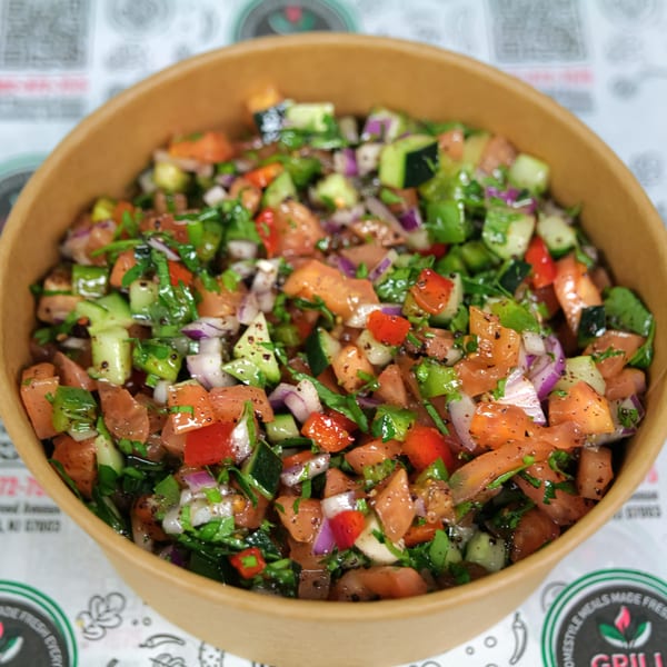Close-up of a fresh salad with diced tomatoes, cucumbers, red onions, and parsley in a brown bowl.